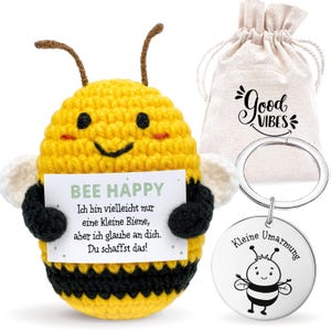 Puede incluir: Una abeja amarilla y negra de ganchillo que sostiene un cartel que dice "BEE HAPPY". Una pequeña bolsa con cordón con "Good Vibes" impreso y un llavero plateado con una ilustración de abeja y las palabras "Kleine Umarmung".