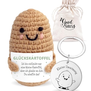 May include: A crocheted potato-shaped plush toy with a smiling face and a sign that reads "GLÜCKSKARTÖFFEL". Includes a drawstring bag with "Good Vibes" text and a keychain with a potato graphic and the words "Kleine Umarmung".