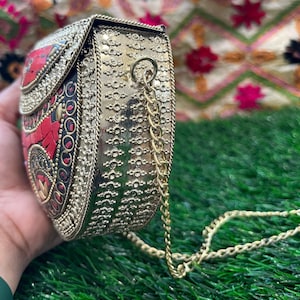 May include: A gold metal clutch purse with a red and black mosaic design and a gold chain strap.