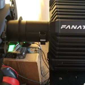 May include: A black Fanatec racing wheel base with a black steering wheel attached. The base has a black and white logo that reads "Fanatec".