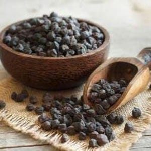 Könnte beinhalten: Eine Holzschale gefüllt mit schwarzen Kichererbsen, daneben eine Holzschaufel, die einige Kichererbsen auf eine Jutestoffoberfläche fallen lässt.