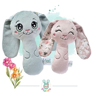May include: Two plush bunny rattle toys for babies. One is light blue with floral print ears and the other is pink with floral print ears. Both have embroidered eyes and a smiling mouth.