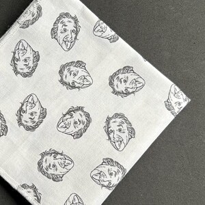 May include: White handkerchief featuring a repeating pattern of a black and white illustration of Albert Einstein with his tongue out. The handkerchief is folded diagonally, with the pattern visible.