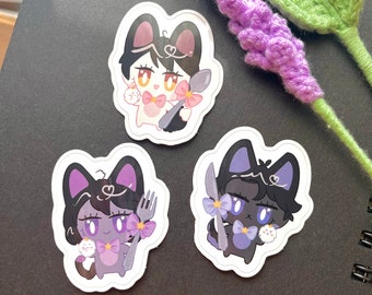 May include: Three black and white cartoon cat stickers with purple and pink accents. Each cat is holding a fork or spoon and has a small white cat in their arms. The stickers are on a black background.