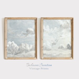 Könnte beinhalten: Zwei gerahmte Vintage-Drucke mit Wolkenlandschaftsgemälden. Das Kunstwerk zeigt flauschige weiße Wolken vor einem hellblauen Himmel. Die Rahmen sind hellbraun. Der Text "Bahama Creation Vintage Prints" befindet sich unten.
