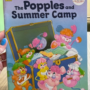 May include: A vintage children's book titled "The Popples and Summer Camp" with illustrations of colorful Popples characters. The cover features a blue trunk surrounded by the Popples. The book is by Peggy Kahn and illustrated by Bobbi Barto.