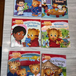 K&ouml;nnte beinhalten: Sechs Kinderb&uuml;cher aus der Reihe "Daniel Tiger's Neighborhood" werden gezeigt. Die Cover zeigen Illustrationen von Daniel Tiger und anderen Charakteren in verschiedenen Umgebungen, mit Titeln wie "Daniel's First Sleepover" und "Big Enough to Help."