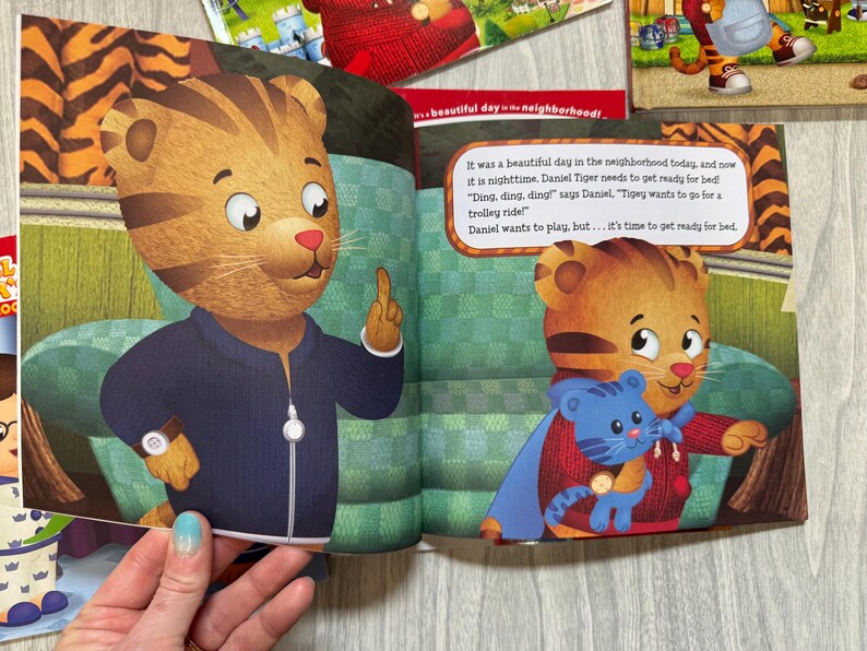 K&ouml;nnte beinhalten: Eine Kinderbuchillustration mit Daniel Tiger, einer animierten Tigerfigur, in einer marineblauen Jacke. Der Text lautet: &bdquo;Es war heute ein wundersch&ouml;ner Tag in der Nachbarschaft, und jetzt ist es Nacht. Daniel Tiger muss sich fertig machen, um ins Bett zu gehen!"