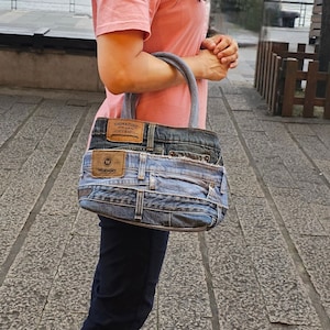 Puede incluir: Un bolso tote de mezclilla hecho de jeans reutilizados. El bolso tiene una etiqueta de cuero marrón con el texto "Signature Levi Strauss" y una etiqueta de cuero marrón con el texto "Wrangler".