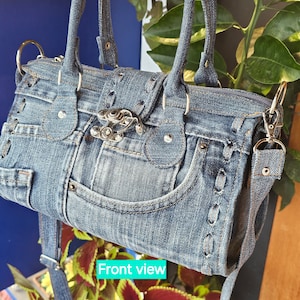May include: A blue denim handbag with a silver buckle and a long strap. The bag has a front pocket and is made from recycled denim.