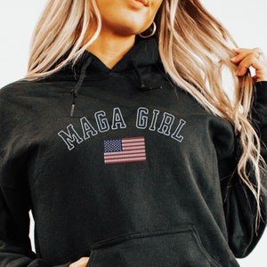 May include: Black hooded sweatshirt with the text "MAGA GIRL" in white outlined letters and an American flag graphic.