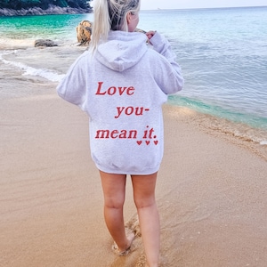 Może przedstawiać: Szara bluza z kapturem z napisem "Love you- mean it." w czerwonych literach i trzema małymi czerwonymi sercami.