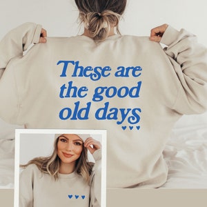 May include: A beige sweatshirt with the text "These are the good old days" in blue lettering and small blue hearts on the back. The front of the sweatshirt has small blue hearts.