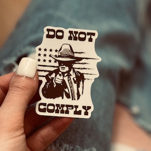 May include: A white sticker with a black and white illustration of a person wearing a cowboy hat and pointing a finger. The text "DO NOT COMPLY" is printed on the sticker.