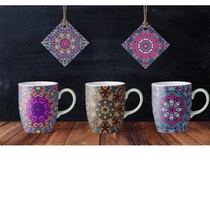 Può includere: Quattro tazze in ceramica bianca con disegni di mandala colorati. Le tazze hanno un manico bianco e sono disposte in fila su una superficie di legno.