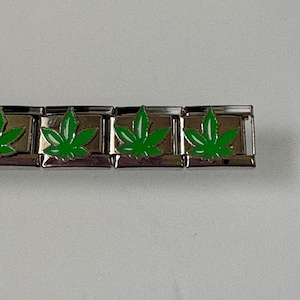 May include: A silver bracelet with rectangular links, each displaying a bright green cannabis leaf design. The leaves have detailed veins, set against a plain background.