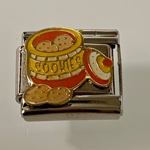 Puede incluir: Un charm de plata con un diseño esmaltado colorido de un tarro de galletas. El tarro es amarillo y naranja con la palabra "COOKIES" en letras doradas. Varias galletas son visibles dentro y fuera del tarro.
