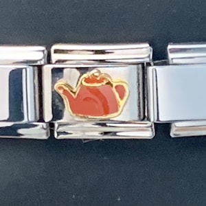 May include: A silver charm bracelet with a red and gold teapot charm. The charm is attached to a silver link on the bracelet.