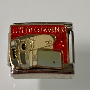May include: Silver charm bracelet charm with a red background and the words "I Love My Camcorder" in white. The charm features a cartoon camcorder with a white body and a gray lens.