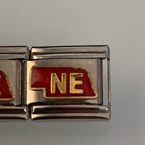 May include: A silver charm bracelet with a red and gold charm that says "NE".