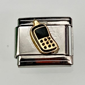 May include: A silver-toned charm with a gold and black cell phone design. The cell phone charm has a black screen and gold buttons. The charm is rectangular with a hinged clasp.