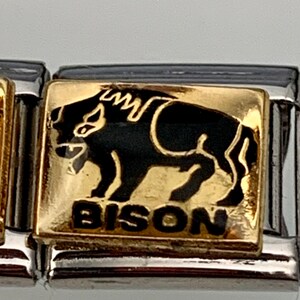 Op de afbeelding: Gouden bedel met een zwart silhouet van een bizon en het woord "BISON" in gouden letters. De bedel is ontworpen voor een bedelarmband.