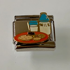 Puede incluir: Un charm de plata con un diseño de esmalte colorido. El charm presenta un plato de galletas, un vaso de leche y una botella de leche con la palabra "MILK". El charm es un accesorio temático de comida.