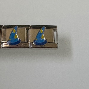 May include: Two silver-toned charm links, each featuring a blue wizard hat with yellow stars. The hats are enamel-filled and have a shiny finish. The charms are likely for a bracelet or necklace.