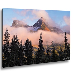 May include: A scenic landscape print featuring a mountain range partially obscured by clouds. The foreground shows dark green evergreen trees, with the mountain peaks visible above the clouds. The sky transitions from pink to blue.