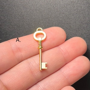 Könnte beinhalten: Ein goldfarbener Schlüsselanhänger mit einem dekorativen, gedrehten Stiel und einer runden Schlaufe oben. Der Schlüssel ist etwa 5 cm lang.