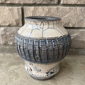 May include: A white ceramic vase with a dark brown band around the middle. The vase has a crackled glaze and a textured design.
