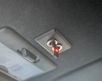May include: A close-up of a grey switch with a red light on, mounted on the ceiling of a car.