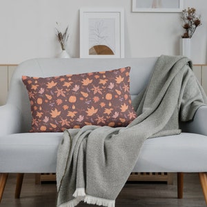 May include: A gray couch with a throw blanket and a decorative pillow with a fall-themed pattern of orange and brown leaves and pumpkins.