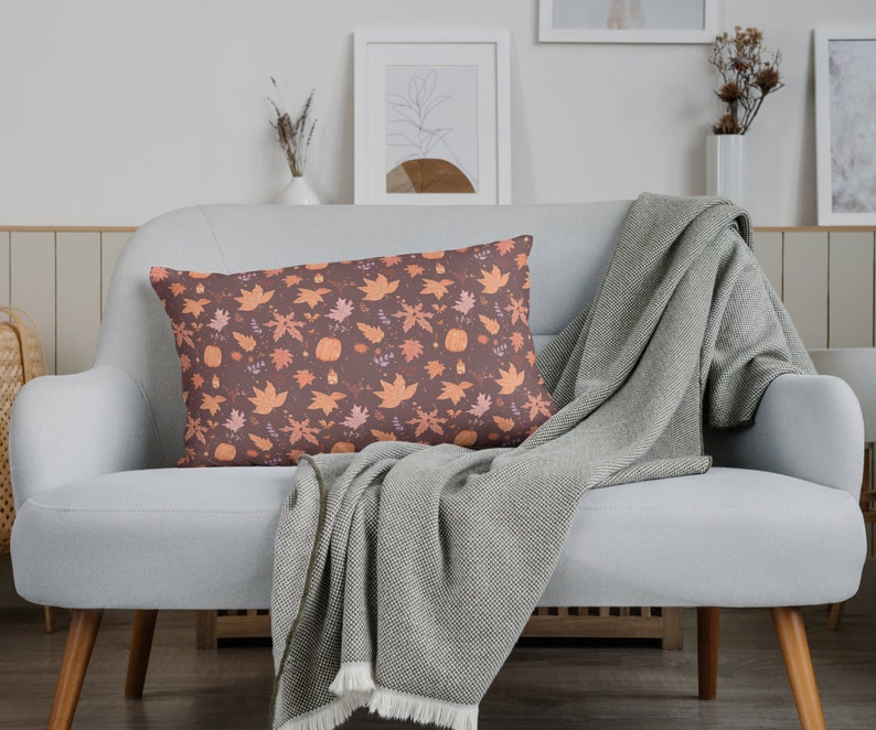 May include: A gray couch with a throw blanket and a decorative pillow with a fall-themed pattern of orange and brown leaves and pumpkins.