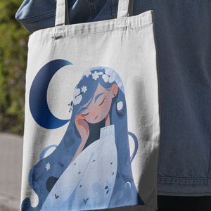 May include: A white tote bag with a blue crescent moon and a cartoon illustration of a woman with blue hair wearing a white dress and a flower crown.