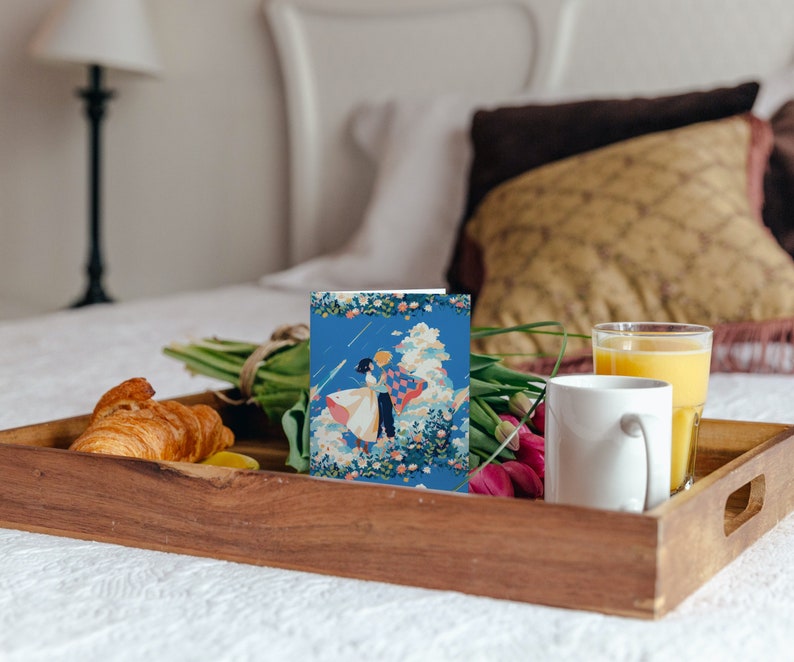 May include: A wooden tray with a white mug, a glass of orange juice, a croissant, a bouquet of tulips, and a card with a blue and white illustration of a couple dancing.