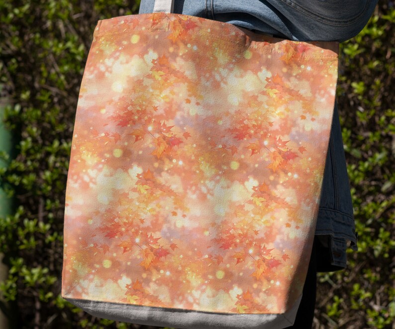 May include: A tote bag with a fall-themed design featuring orange, yellow, and red leaves on a white background with a subtle shimmer effect.