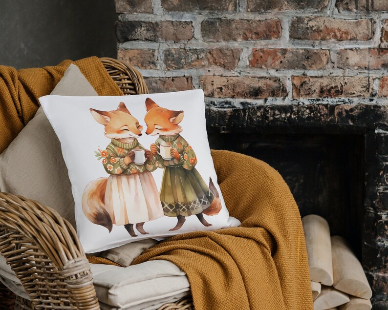 May include: A white throw pillow with a watercolor illustration of two foxes holding mugs. The foxes are wearing sweaters and skirts. The background is a brick wall.