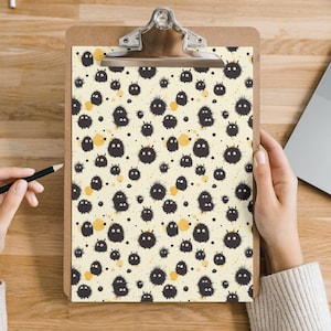 May include: A clipboard with a white background and a black and white pattern of fuzzy creatures. The creatures are all facing the same direction and have small black eyes. The background is covered in small yellow dots.