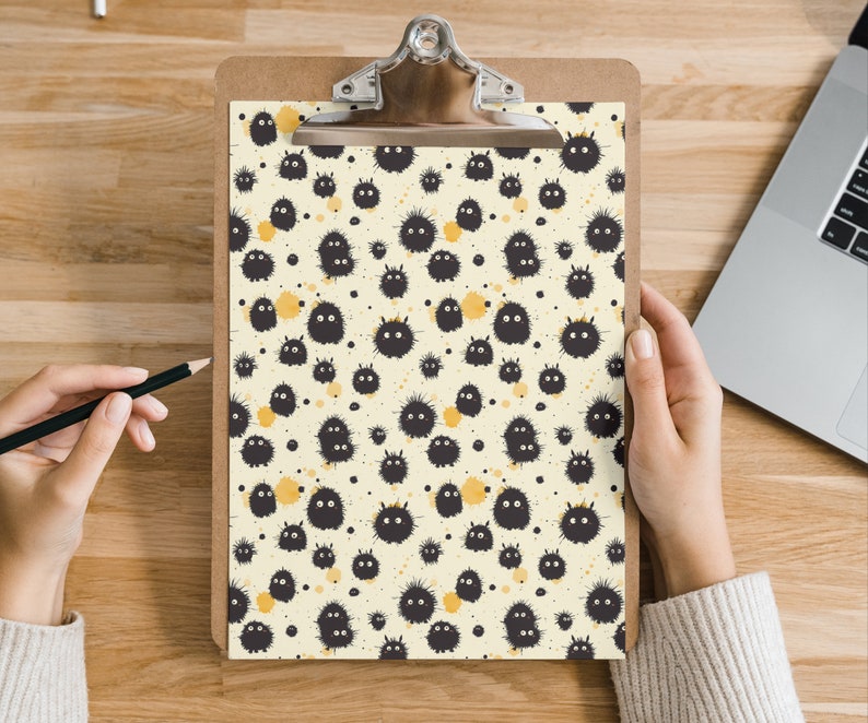 May include: A clipboard with a white background and a black and white pattern of fuzzy creatures. The creatures are all facing the same direction and have small black eyes. The background is covered in small yellow dots.