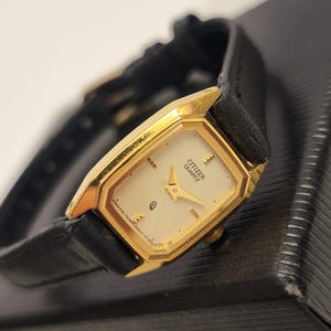 May include: A Citizen Quartz wristwatch featuring an octagonal gold-tone case and a cream-coloured dial with gold-tone hands and hour markers. The watch has a black leather strap and a small crown on the side. The dial displays the text Citizen Quartz.