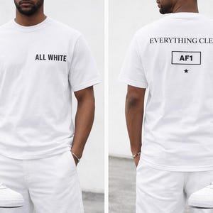 Peut inclure: T-shirt blanc avec "ALL WHITE" imprimé sur le devant et "EVERYTHING CLEAN" au dos. Le t-shirt est associé à un short blanc et des baskets blanches. Le dos du t-shirt comporte également "AF1" dans un encadré et une étoile.