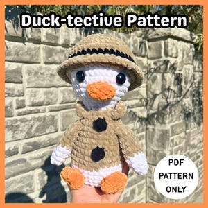 May include: A crocheted duck wearing a tan safari hat and coat with black buttons. The duck has a white head, an orange beak and feet. The text "Duck-tective Pattern" is at the top, and "PDF PATTERN ONLY" is in a circle at the bottom.