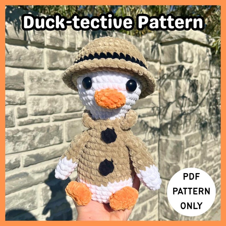 May include: A crocheted duck wearing a tan safari hat and coat with black buttons. The duck has a white head, an orange beak and feet. The text "Duck-tective Pattern" is at the top, and "PDF PATTERN ONLY" is in a circle at the bottom.