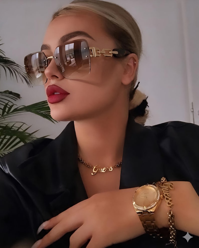 May include: Brown gradient sunglasses with gold accents and a gold chain necklace and bracelet with the word "Guess". A gold watch with a gold band is also visible.