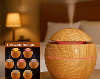 May include: A wood-grain essential oil diffuser with a dome-shaped top and a red interior. The diffuser has a power button and a pink accent line. A small display shows the LED light options. The text on the display reads "LED Colorful Mild Light".
