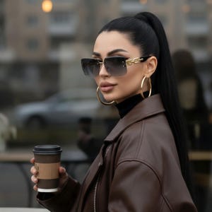 May include: Square-framed sunglasses with gradient lenses and gold accents. The sunglasses are paired with large gold hoop earrings. The person is wearing a brown leather jacket and holding a coffee cup.