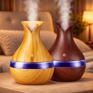May include: Two wooden-look essential oil diffusers. One is light-colored, the other is dark. Both have a blue band and a power button. Steam rises from the top of each diffuser, suggesting they are in use. The diffusers are on a wooden surface.