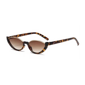 K&ouml;nnte beinhalten: Katzenaugen-Sonnenbrille mit einem braunen Schildpattmuster-Rahmen und einem d&uuml;nnen goldfarbenen Metallrand an der Oberseite der Gl&auml;ser. Die Gl&auml;ser haben einen braunen Farbverlauf, der von einem dunkleren Ton oben zu einem helleren Ton &uuml;bergeht.