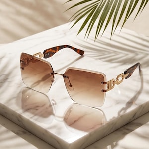 May include: Brown gradient sunglasses with a gold metal frame and chain detail on the temples. The sunglasses have a square shape and a tortoiseshell pattern on the arms. The lenses are a gradient brown color.